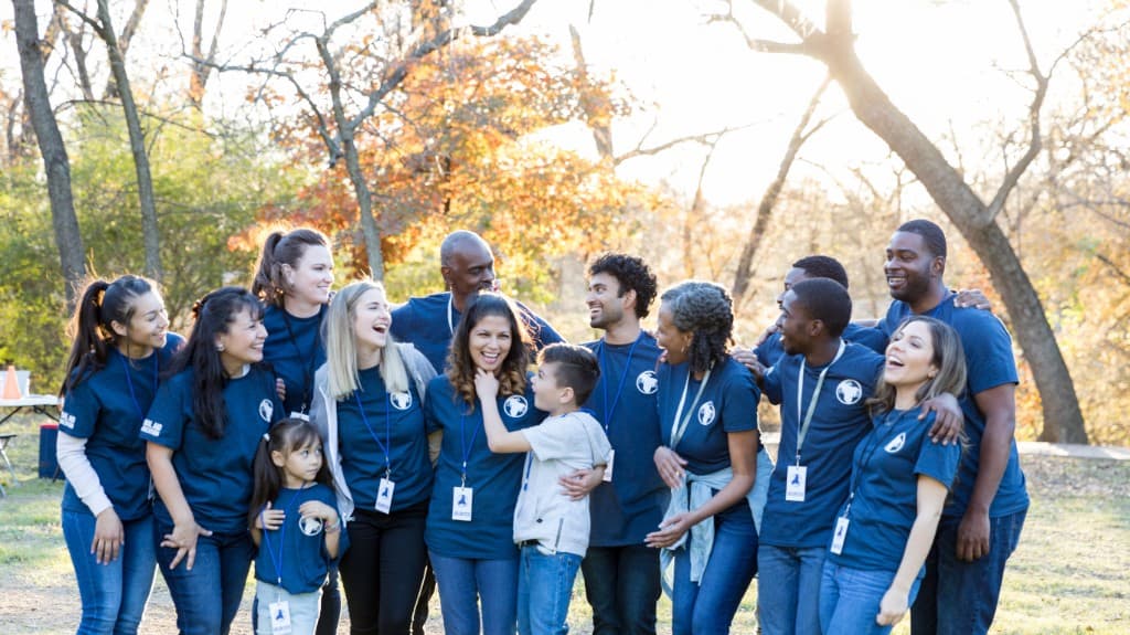 A diverse team wearing matching shirts, smiling together outdoors.